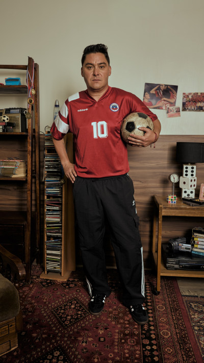 A young man wearing a red soccer jersey with the number 10 stands in a room filled with shelves of vinyl records and other memorabilia.