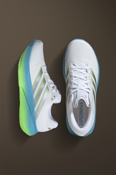 A pair of white and green athletic shoes with laces, resting on a dark brown background.