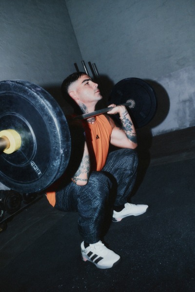A person in an orange shirt and black pants is lifting a heavy barbell in a dimly lit gym setting.