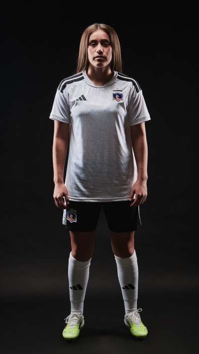 A person wearing a gray soccer jersey and shorts, standing in a dark background.