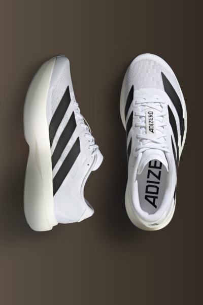 A pair of white and black athletic shoes with the Adidas logo prominently displayed on a dark background.