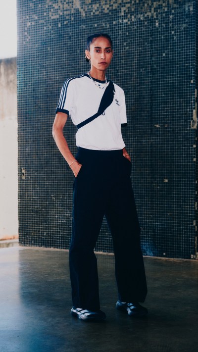 The image shows a person wearing a white t-shirt and black pants, standing in front of a blue tiled wall.