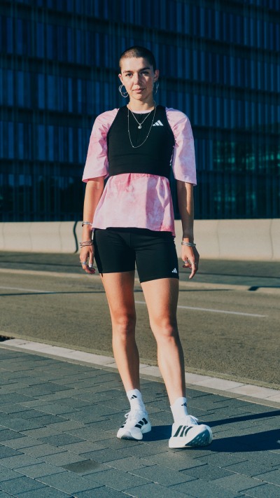 A person wearing a pink and black athletic outfit stands on a paved surface with a blue building in the background.