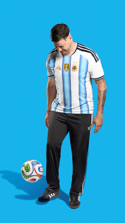 A muscular man wearing an Argentina national team jersey stands next to a soccer ball against a bright blue background.
