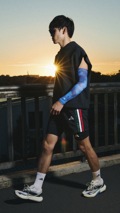 A young man in athletic clothing stands on a wooden deck overlooking a scenic sunset landscape.