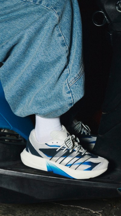 The image shows a close-up view of a person's feet wearing a pair of white and blue sneakers, with the lower part of their jeans visible in the background.