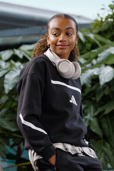 A young woman with curly hair wearing a black and white athletic top stands in front of a lush, green background with a body of water visible in the distance.
