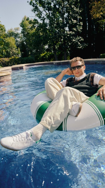A person in casual attire relaxing on a floating pool chair in a serene outdoor setting with lush greenery and a clear blue pool.