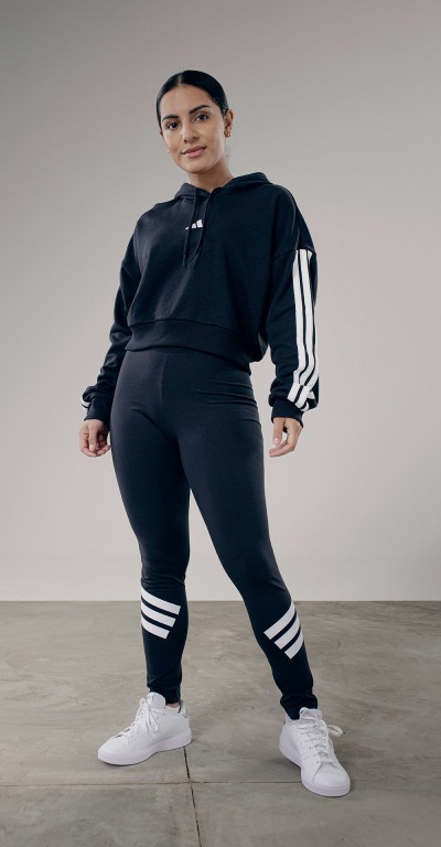 A person wearing a black athletic outfit with white stripes, standing in a plain, light-colored room.
