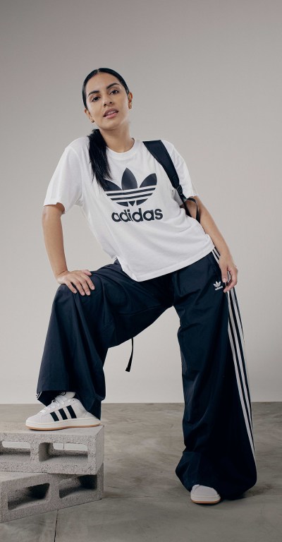 A person wearing an Adidas t-shirt and pants is sitting on a wooden pallet against a plain background.