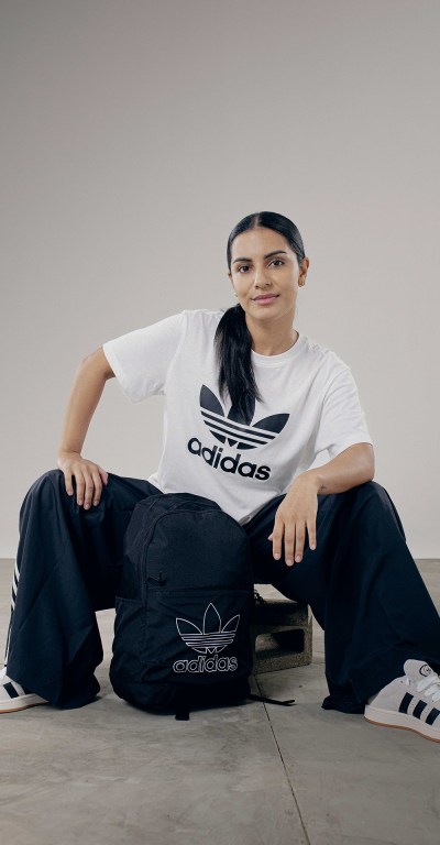 A person wearing an Adidas t-shirt and pants is sitting on the floor against a plain background.