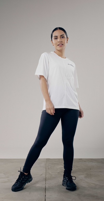 A young person wearing a white t-shirt and black leggings stands in a plain, gray-toned setting.
