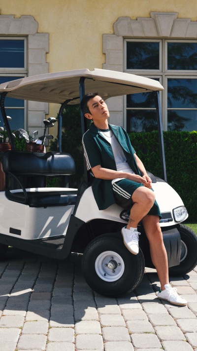 A person is sitting in a golf cart on a paved surface, with a building visible in the background.