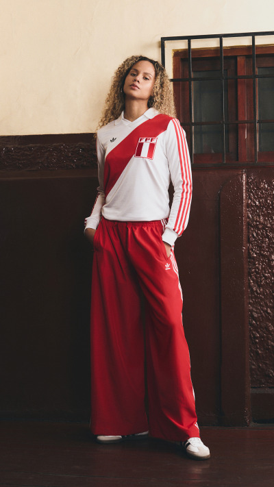 A young woman with curly hair stands in a red and white athletic outfit against a dark background.