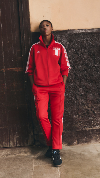 A person wearing a red tracksuit stands in front of a wooden wall.