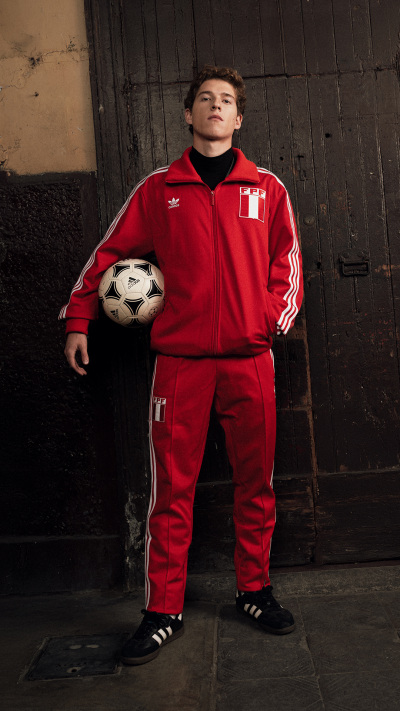 A young man wearing a red sports uniform is standing in a dimly lit indoor setting, holding a soccer ball.
