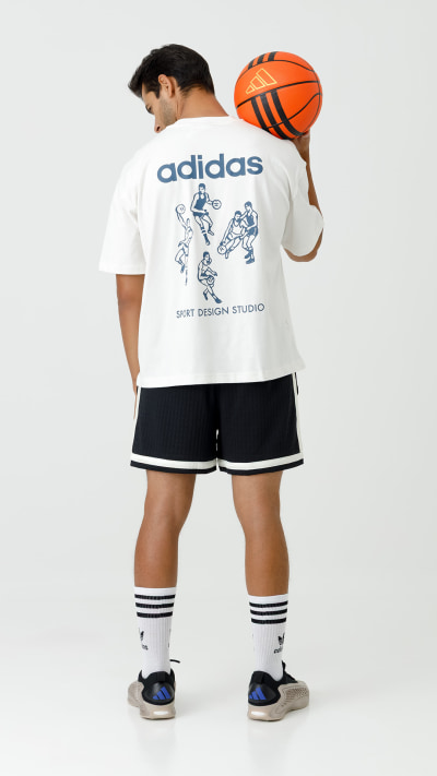 A person wearing an Adidas t-shirt and shorts, holding a basketball, stands against a plain white background.