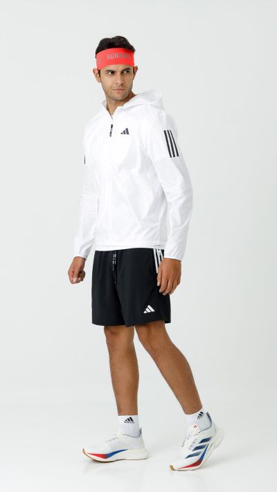 A young person wearing a white athletic jacket, black shorts, and red headband, standing against a plain white background.