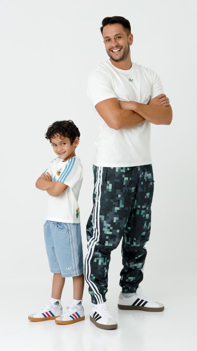 A smiling man stands next to a young boy wearing casual clothing against a plain white background.