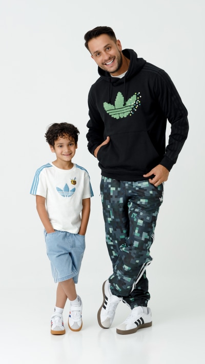 A man wearing a black hoodie with the Adidas logo and a young boy wearing a white t-shirt and light blue shorts stand together against a plain white background.