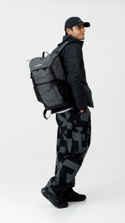 A person wearing a black jacket, cap, and backpack stands in a plain white background.