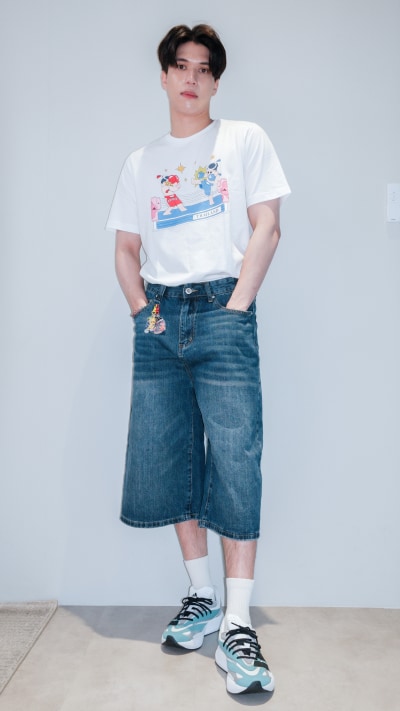 A person wearing a white t-shirt with a graphic design, blue denim shorts, and colorful sneakers stands against a plain white background.