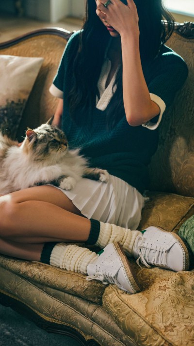 A person in a black top is lying on a couch, petting a fluffy white cat.