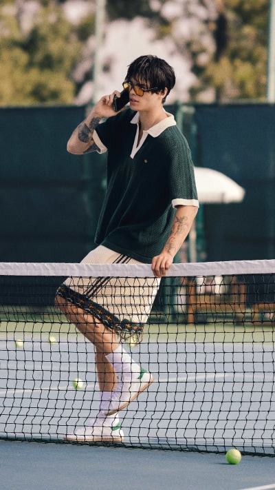 A person in a green shirt is standing on a tennis court, holding a tennis racket and preparing to hit a tennis ball.
