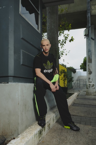 A person wearing a black shirt with a logo, sitting on a concrete step in front of a building with a glass window.