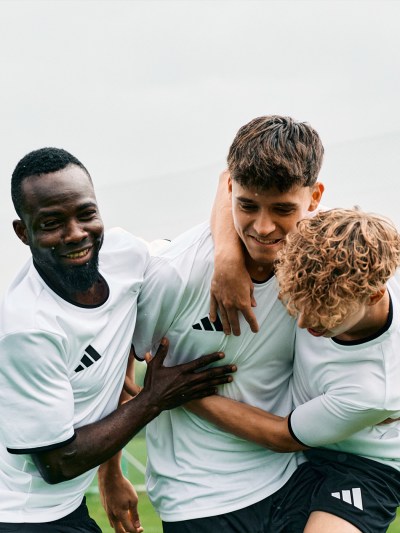Three young men in sports uniforms embracing and smiling against a blurred outdoor background.