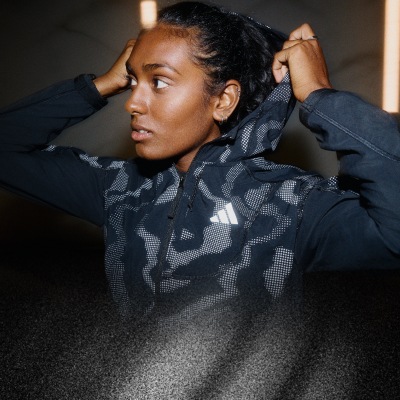 Una persona che indossa una giacca con motivo di colore scuro sembra essere in un ambiente poco illuminato, con lo sfondo che sembra essere una superficie piana e scura.