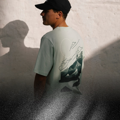 Človek v čiernej čiapke stojí v popredí a tieň vrhaný na stenu za nimi vytvára zaujímavý vizuálny kontrast.