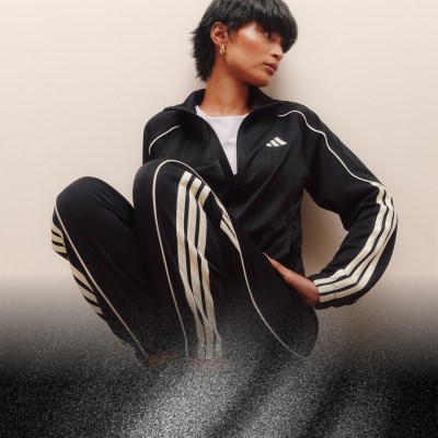 Una persona che indossa una giacca sportiva a righe bianche e nere e pantaloni è in piedi in un ambiente poco illuminato.