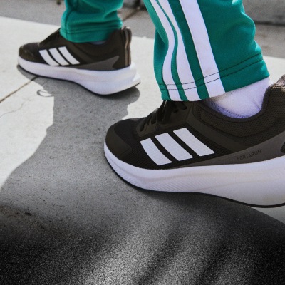 Na obrázku sú čiernobiele tenisky so zelenými a bielymi prúžkami po bokoch, ktoré stoja na betónovom povrchu.