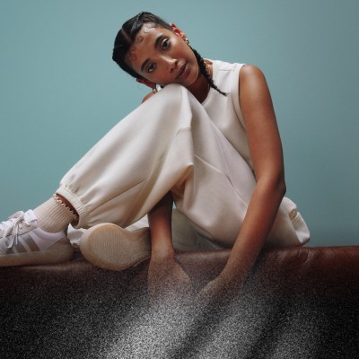 Una persona con un outfit bianco si siede su una superficie scura su uno sfondo verde acqua, per esprimere la propria personalità pensosa e pensierosa.