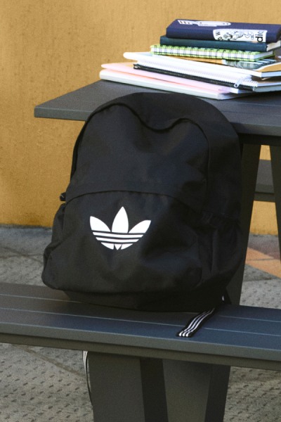 Una mochila negra de adidas sobre un escritorio, rodeada de varios libros de texto y cuadernos.