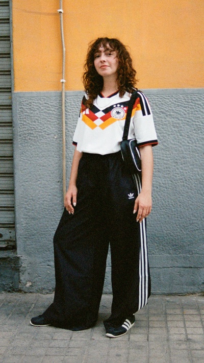 A person wearing a white and black jersey with a German flag design, standing in front of a yellow and gray wall.