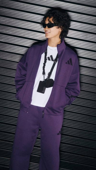 A person wearing a purple suit and sunglasses stands in front of a black metal shutter backdrop.