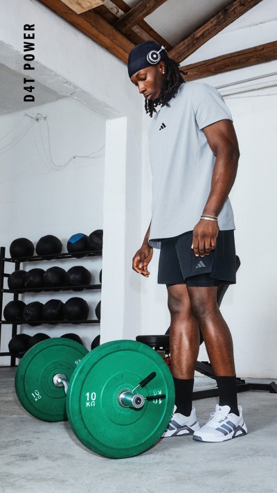 Eine Person in Sportbekleidung hebt eine Reihe grüner Gewichte in einem Fitnessstudio, wobei im Hintergrund Regale mit zusätzlichen Gewichten zu sehen sind.