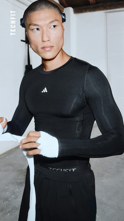 Eine Person, die ein schwarzes Oberteil und eine schwarze Hose trägt, steht in einem Raum mit einer Decke und Wand aus Holz.