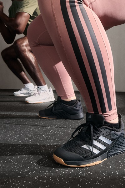 The image shows a person's lower body wearing pink and black striped leggings and black athletic shoes, standing on a textured floor.