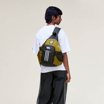 A young person wearing a white t-shirt and black pants, carrying a yellow and black backpack, stands against a plain light-colored background.