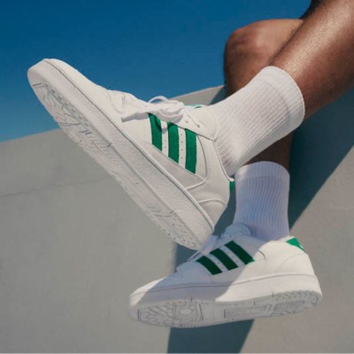 A pair of white and green sneakers against a bright blue sky, with the person's legs visible in the foreground.