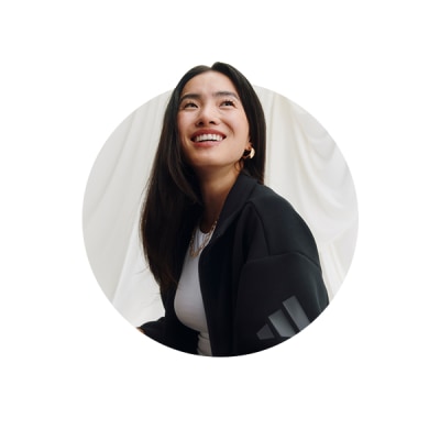 A smiling woman with long dark hair wearing a black jacket stands against a plain white background.