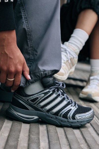 L'immagine mostra la parte inferiore del corpo di una persona, con un paio di sneaker grigie e calzini bianchi visibili in primo piano, su uno sfondo scuro.