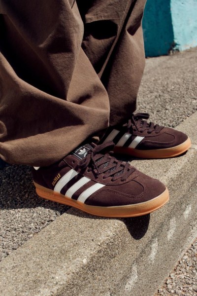 Un paio di sneaker marroni e bianche posano su una superficie sterrata, con un panno beige sullo sfondo.