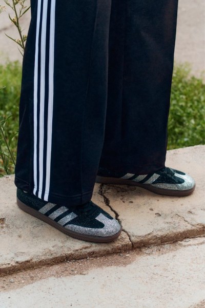 L'immagine mostra un paio di pantaloni neri con strisce bianche sui lati e un paio di sneaker grigie e bianche su una superficie di cemento con uno sfondo erboso.