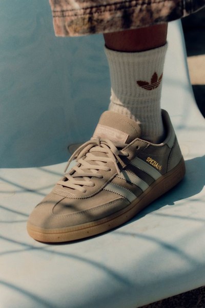 L'immagine mostra un paio di sneaker adidas Samba beige e marroni con calzini bianchi su uno sfondo blu.