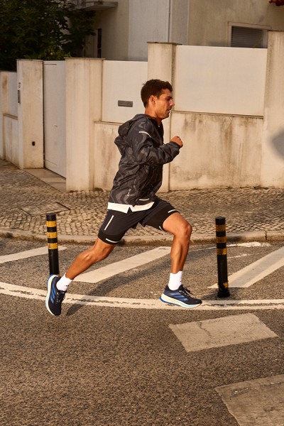 A person in athletic clothing is running on a crosswalk in an urban setting, with buildings and other structures visible in the background.