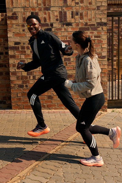 Two people in athletic clothing are engaged in a physical activity, with one person appearing to be defending against the other's movements in front of a brick wall background.